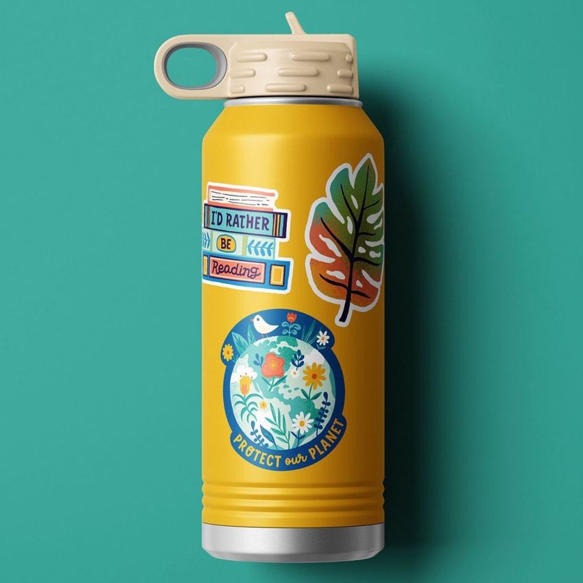 Powder coated 32 oz. water bottle mockup with colorful stickers, including a floral globe and leaf, on a teal background.