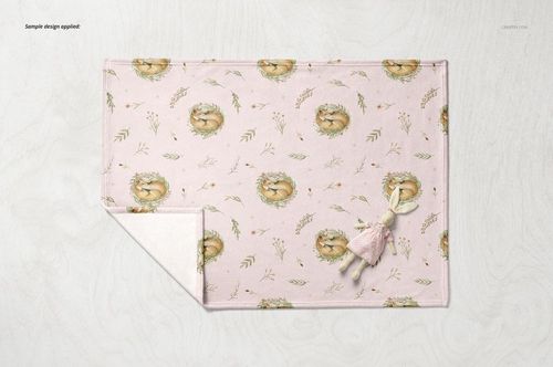 Baby blanket mockup featuring a light pink fleece fabric with fox and wreath motifs, displayed with a small plush toy.