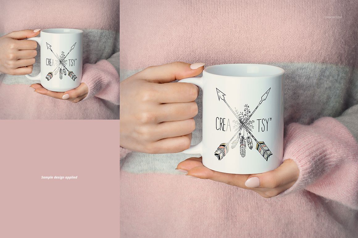 Front view of a white ceramic mug held by hands, featuring a sample arrow and feather design, against a pink and gray sweater.