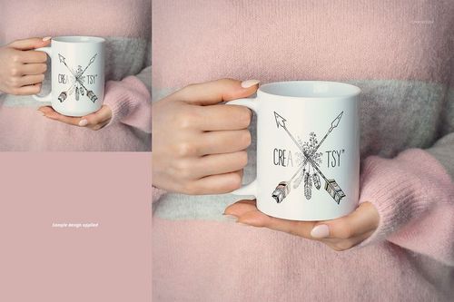 Front view of a white ceramic mug held by hands, featuring a sample arrow and feather design, against a pink and gray sweater.