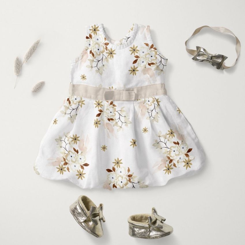 Baby dress mockup featuring a white dress with watercolor floral pattern, matching headband, and gold baby shoes on a light background.