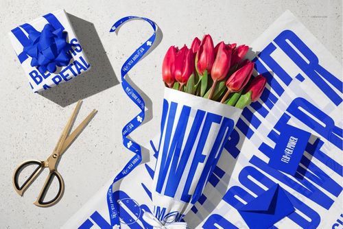 PSD mockup featuring tulips bouquet in printed tissue wrapping paper, blue ribbon, scissors, and a gift box on a tabletop.