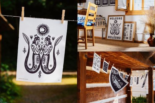 Folk art print with two winged figures in black ink clipped to a clothesline outdoors, sunlight filtering through trees.