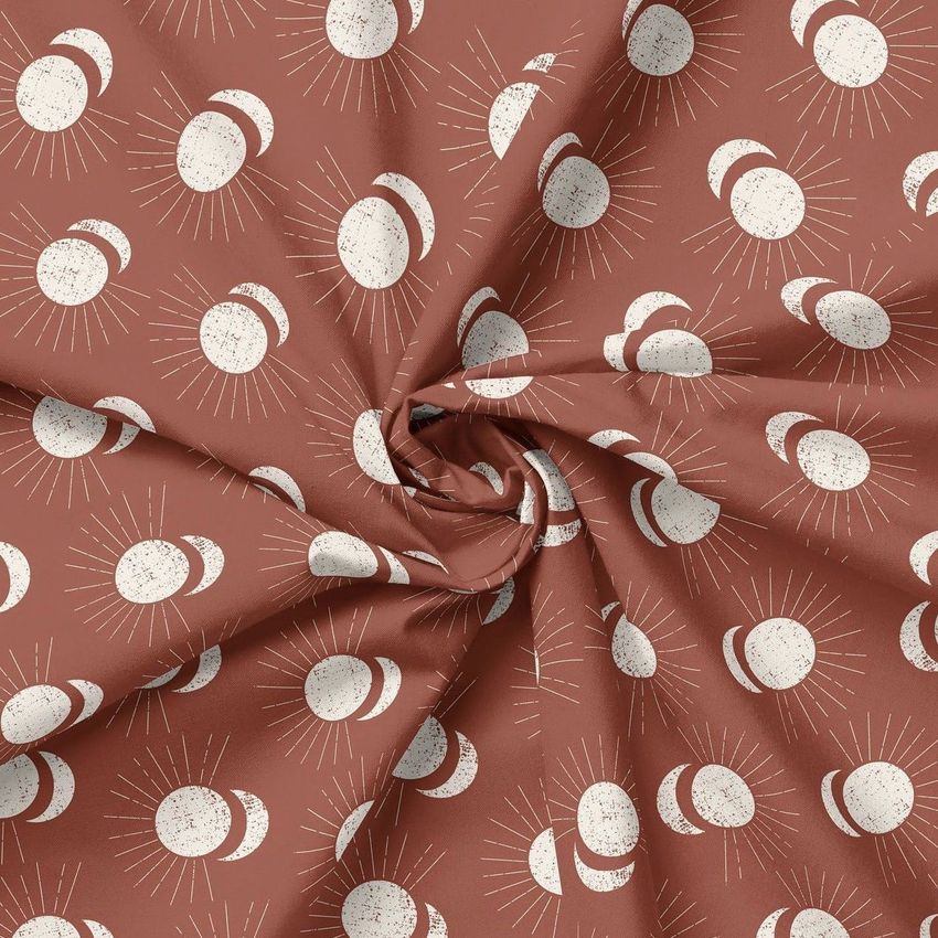 Creased fabric mockup featuring a rust-colored textile with a repeating pattern of white sun and moon phases, viewed from above.