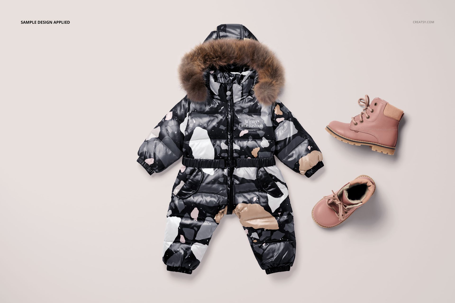Baby snow suit mockup with a fur-trimmed hood, black and beige design, shown flat with two pink boots on a light background.