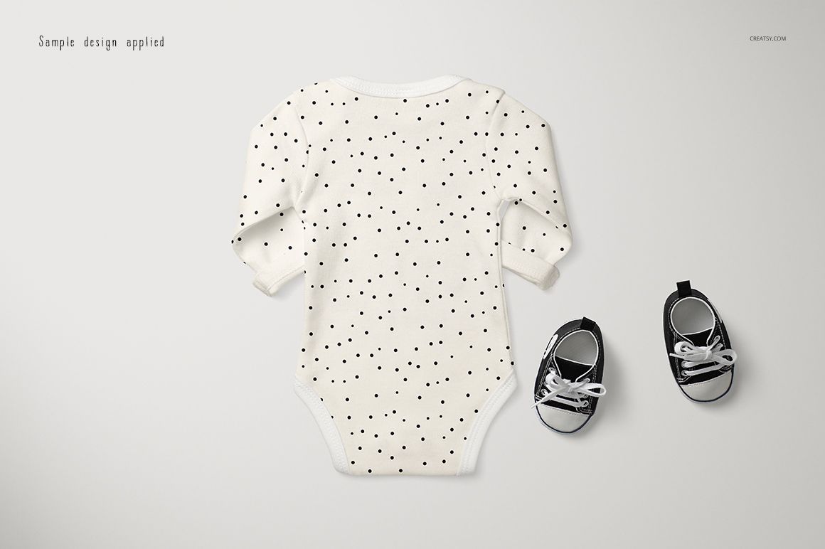Longsleeve baby onesie mockup with black polka dot pattern, shown from the back on a light surface next to black baby shoes.