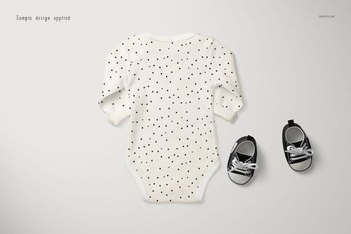 Longsleeve baby onesie mockup with black polka dot pattern, shown from the back on a light surface next to black baby shoes.