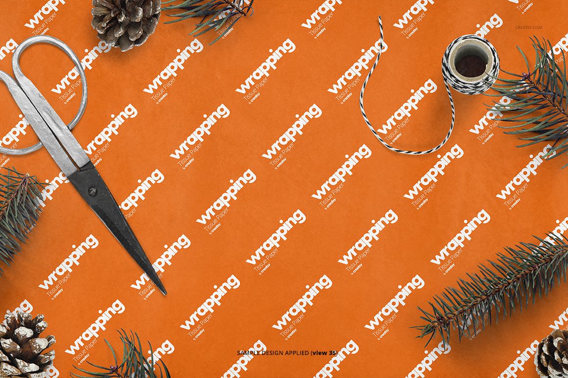 Orange wrapping tissue paper mockup shown from top view, surrounded by scissors, twine, pinecones, and fir branches.