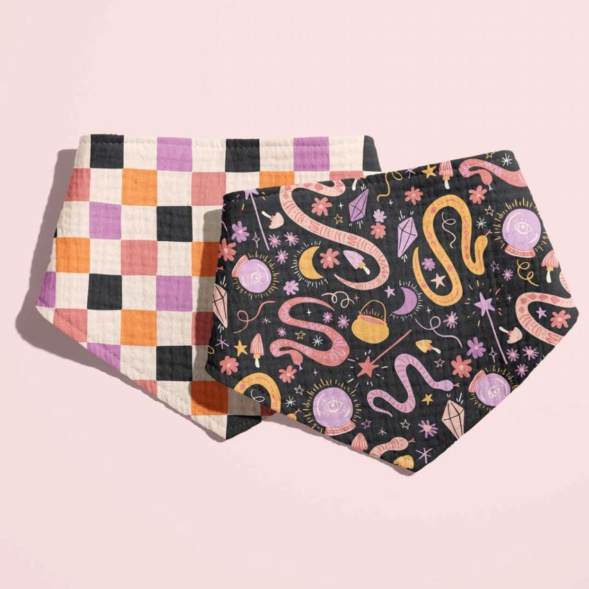 Two baby muslin bandana mockups are displayed side by side on a light pink background, one with a colorful checkered pattern and the other with a whimsical snake and moon design in pink, purple, and orange tones.