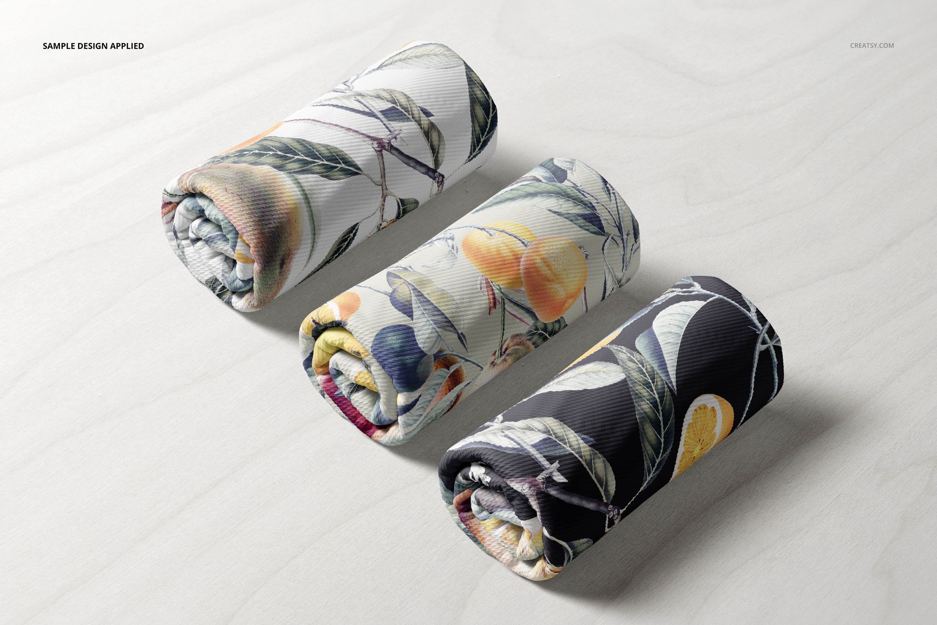 Rolled bullet fabric mockups featuring colorful fruit and leaf designs, displayed side by side on a pale wood background.