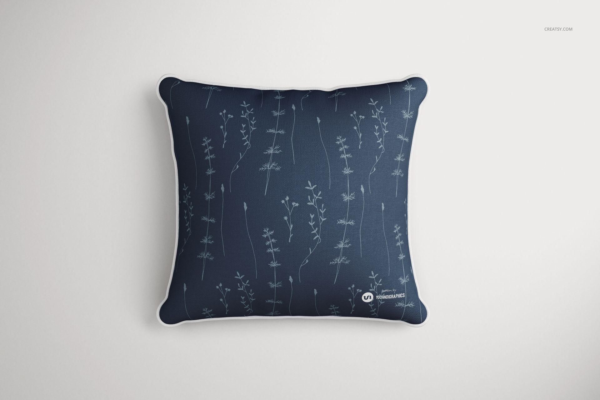 Mockup of a square cushion with white piping, decorated with thin floral stems on a navy blue fabric, top view.