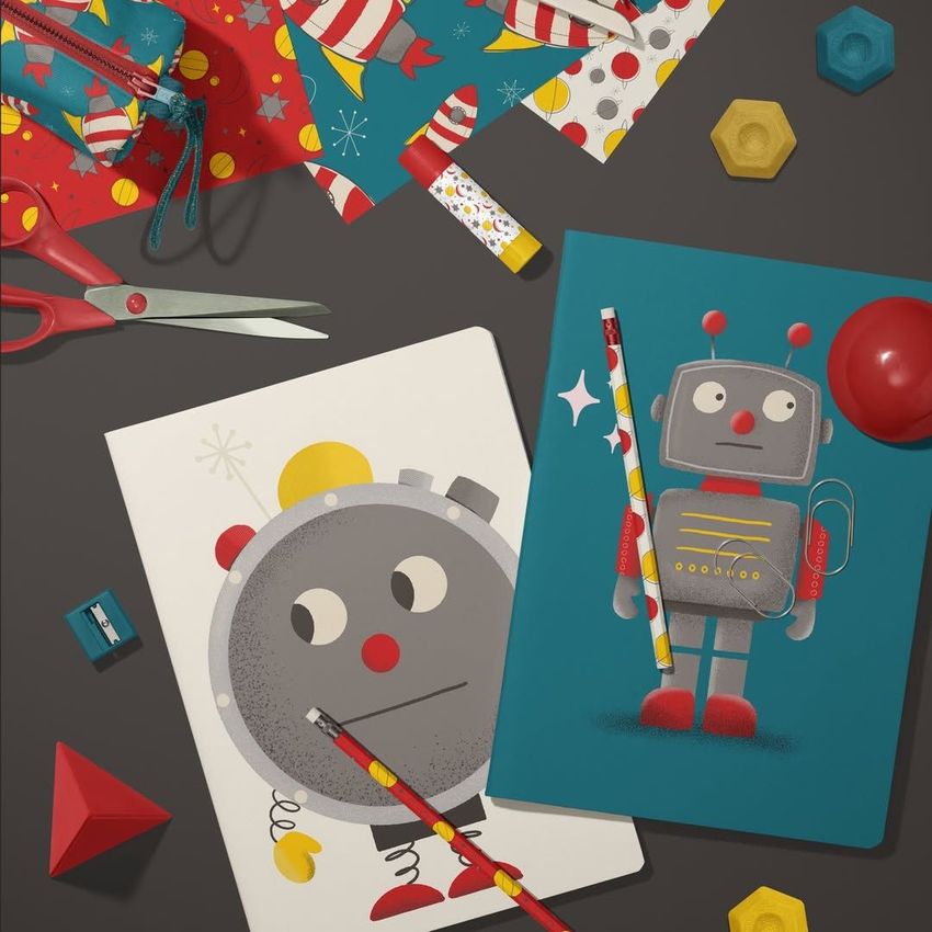 Stationery mockup featuring two A4 notebooks with robot illustrations, colorful pencils, scissors, and geometric props on a dark surface.
