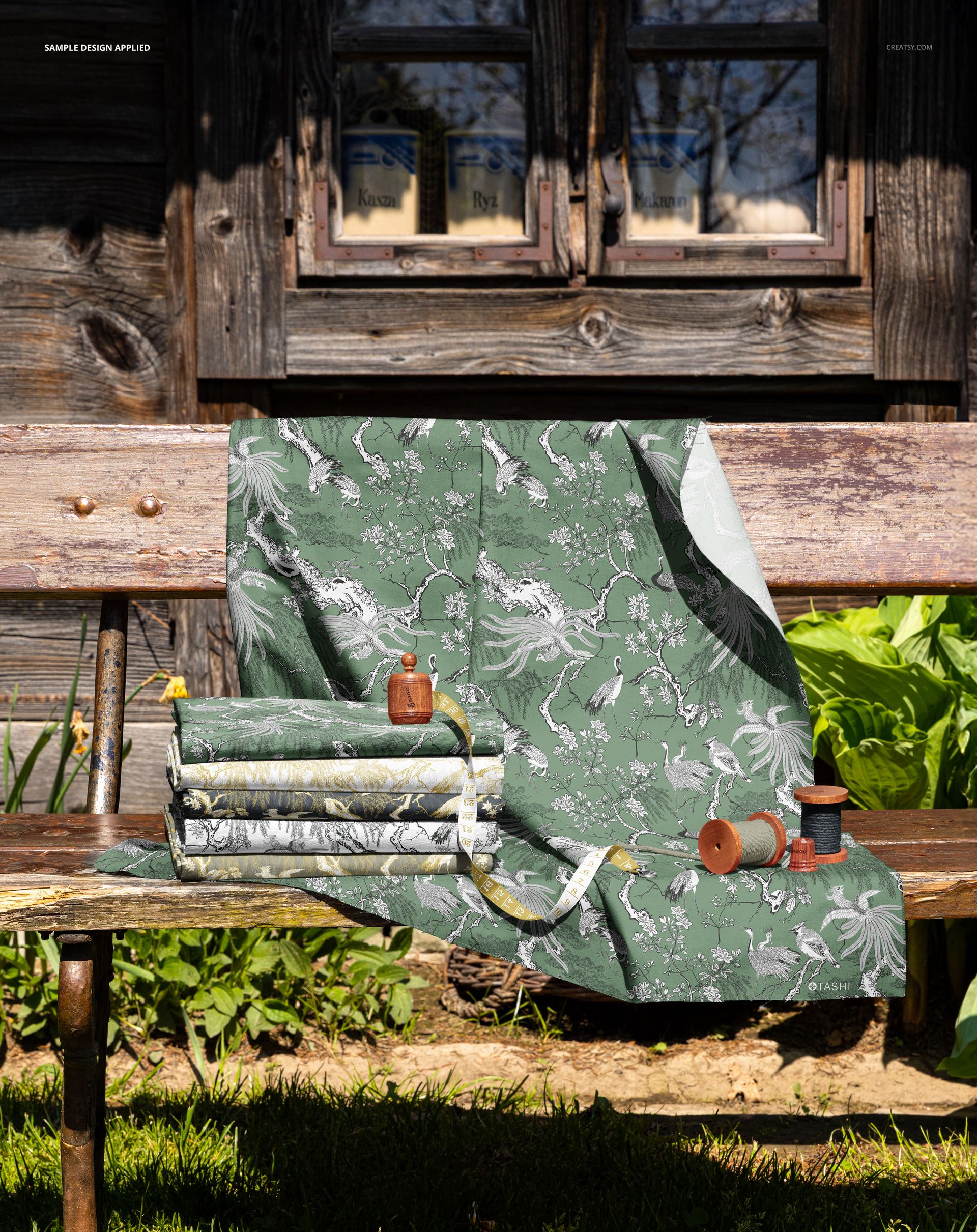 PSD mockup showing folded and draped fabrics with nature-inspired designs on a wooden bench in a garden setting.