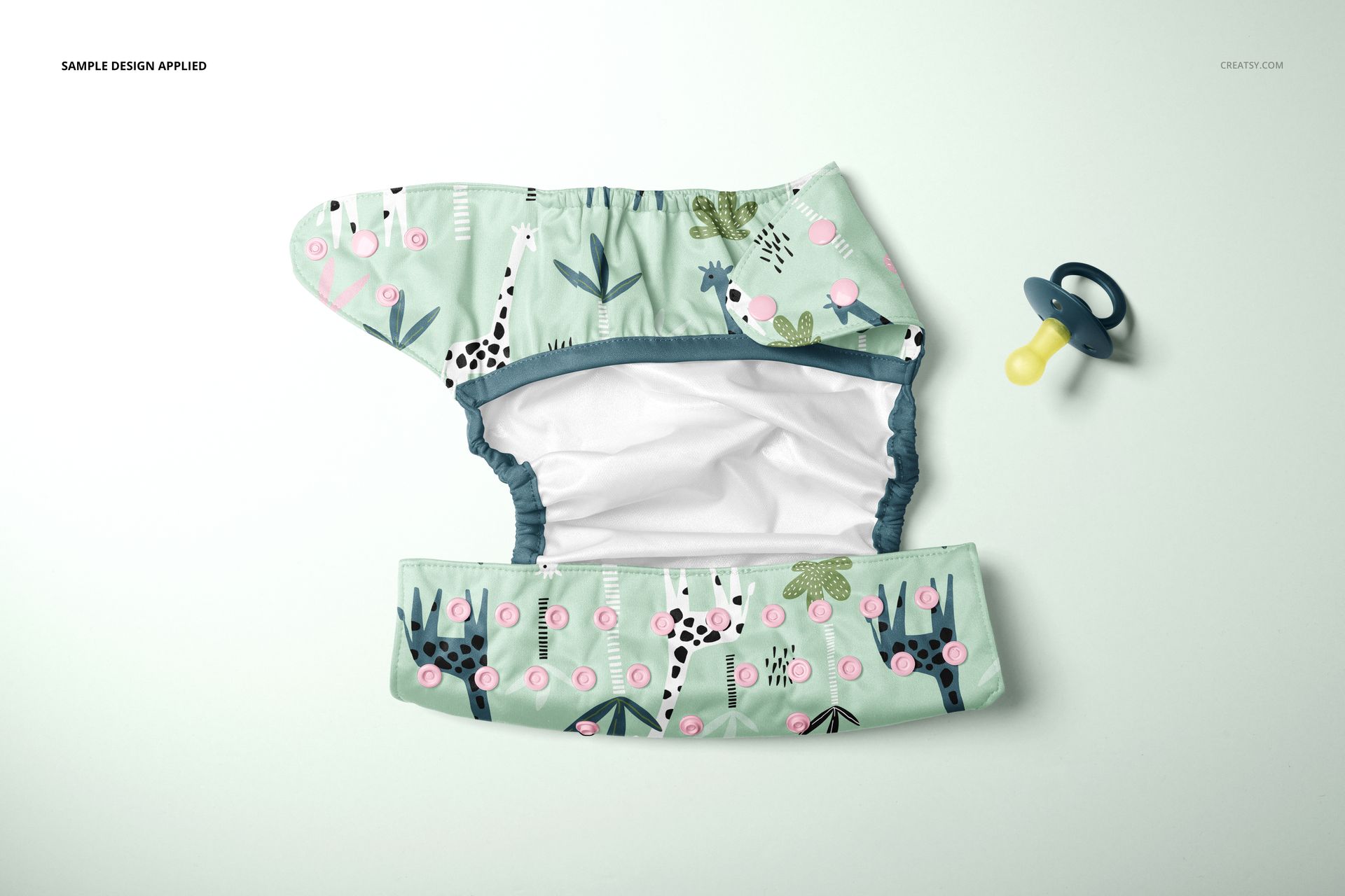 Top view of a reusable baby cloth diaper mockup featuring a whimsical animal pattern and a pacifier nearby.