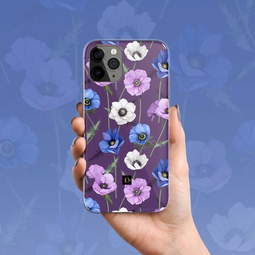 Hand holding an iPhone 11 Pro with a clear case featuring a colorful floral pattern on a purple background, set against a matching floral backdrop.