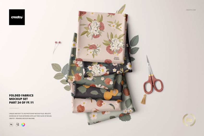 Folded fabrics mockup showing layered textiles with colorful prints, floral motifs, and sewing accessories nearby.