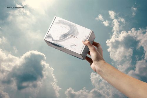 Rectangular packaging box mockup held in a hand, featuring a minimal pattern, set against a cloudy sky background.