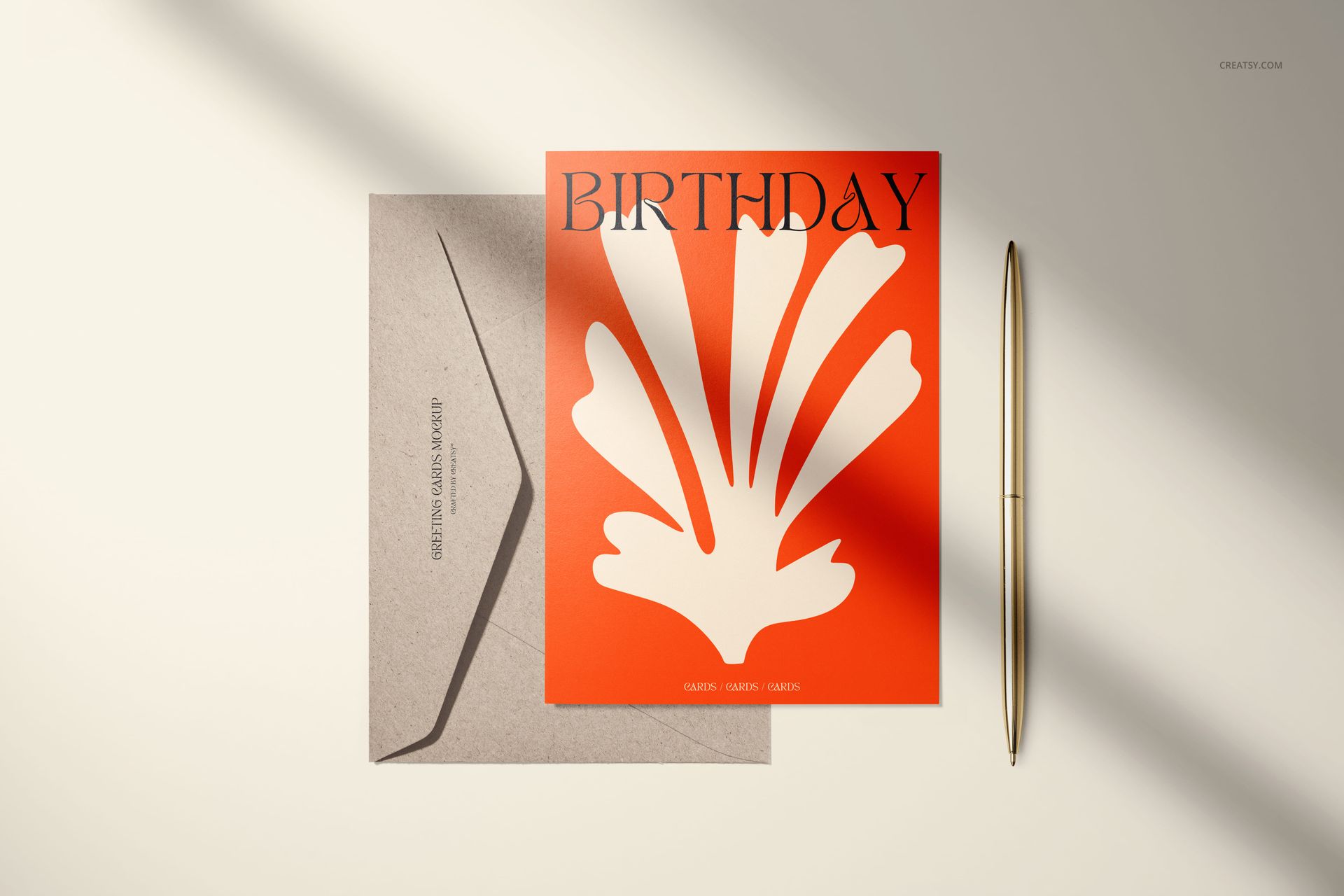 5x7 greeting card mockup featuring an orange card with white abstract pattern, brown envelope, and gold pen on beige background.