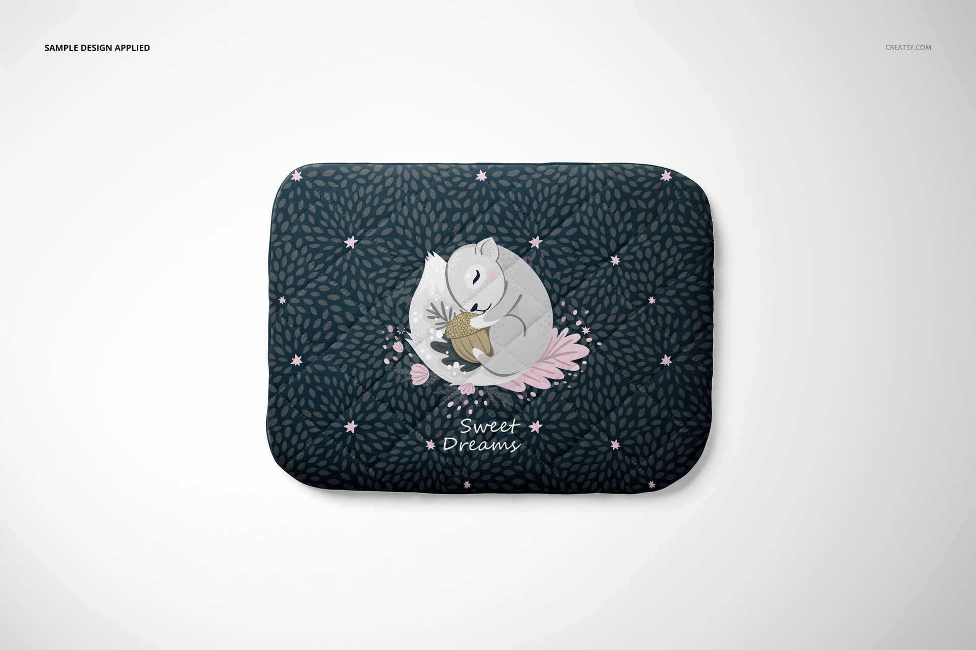 Mockup of a rectangular baby pillow displaying a whimsical sleeping animal design and leafy pattern on a dark surface.
