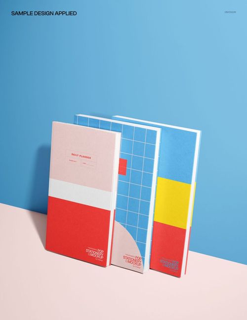 PSD mockup featuring three upright planners with red, blue, and yellow covers, arranged on a two-tone background.