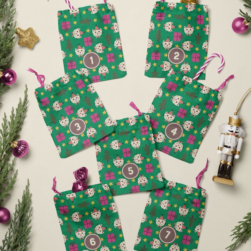 Drawstring sacks advent calendar mockup featuring seven green fabric bags with cat faces, numbers, and festive patterns on a cream surface.