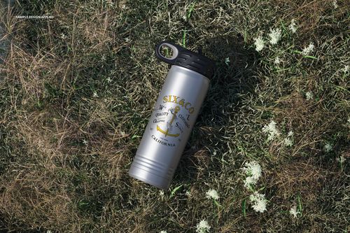 20 oz. stainless steel bottle mockup featuring a black cap and decorative print, placed on grassy ground with flowers.