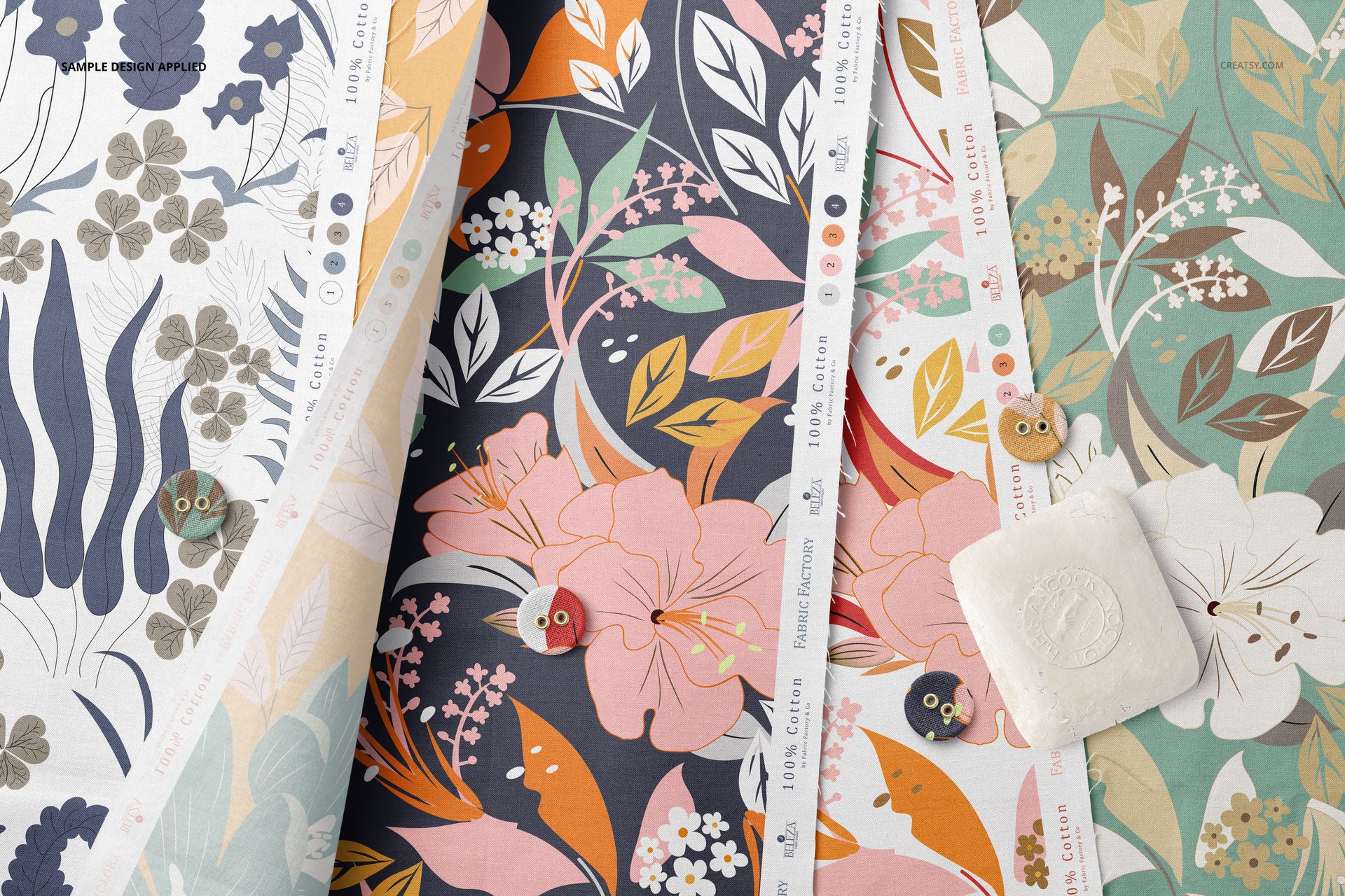 Cotton fabric mockup with multiple folded pieces in assorted botanical prints, top perspective with buttons and soap.