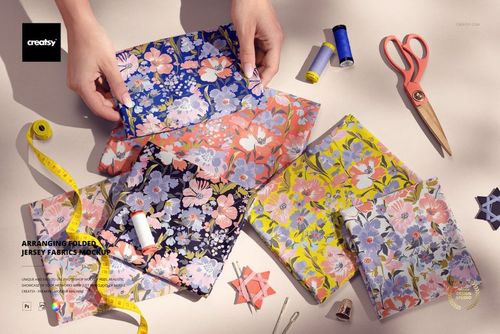 PSD mockup showing assorted floral patterned jersey fabrics laid out with measuring tape, thread, and sewing accessories.