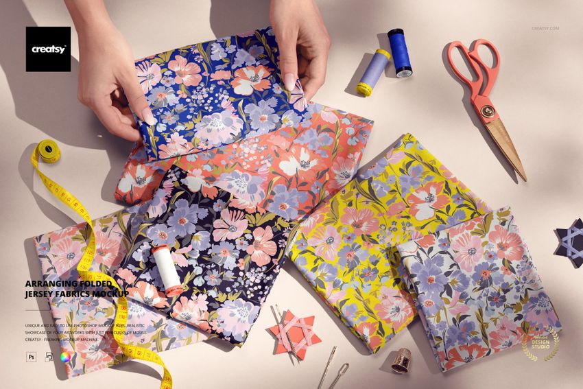 PSD mockup showing assorted floral patterned jersey fabrics laid out with measuring tape, thread, and sewing accessories.