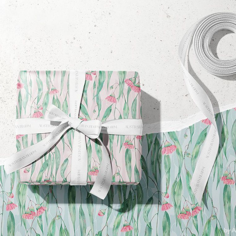 Gift box mockup wrapped in floral patterned paper with pink flowers and green leaves, tied with white ribbon on a light surface.