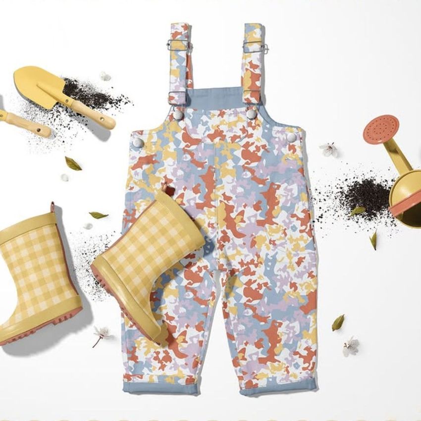 Kids dungarees mockup with a colorful confetti pattern displayed flat on a white surface, surrounded by gardening props.