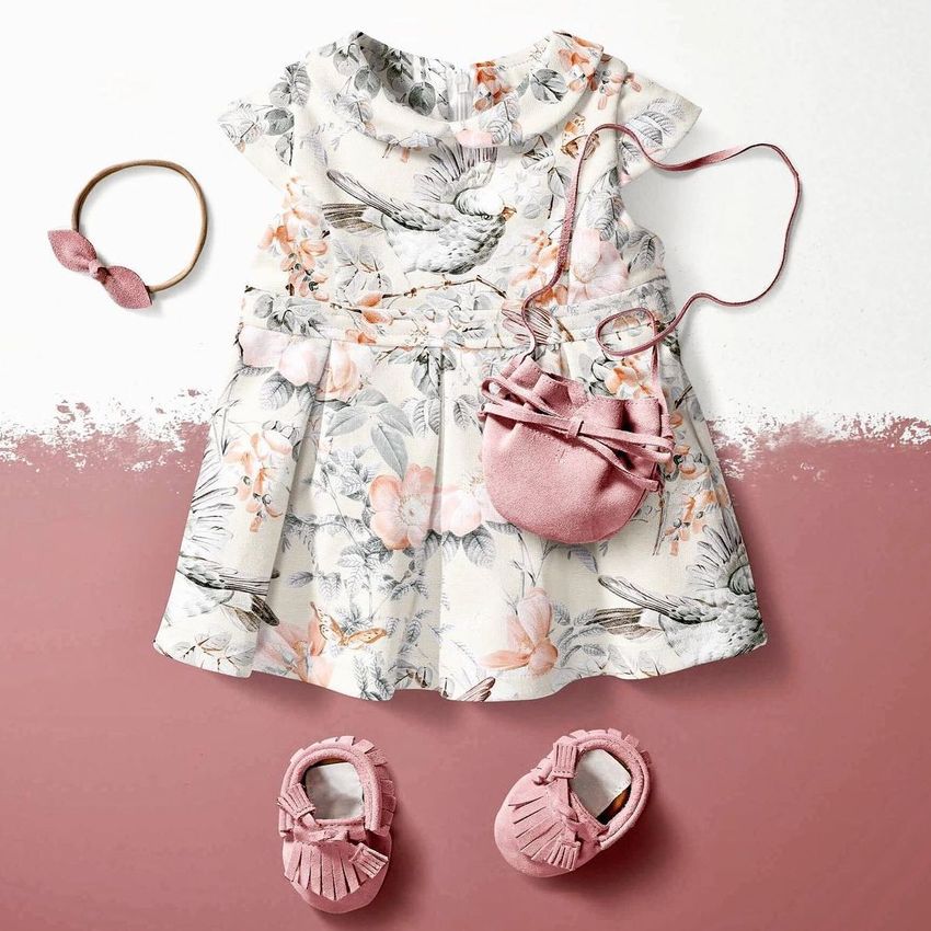 Baby dress mockup with a floral and bird pattern, styled with pink moccasins, a small purse, and a matching headband on a two-tone background.