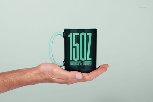 PSD mockup featuring a 15oz mug in black and mint green, shown from the side, supported by a human hand.