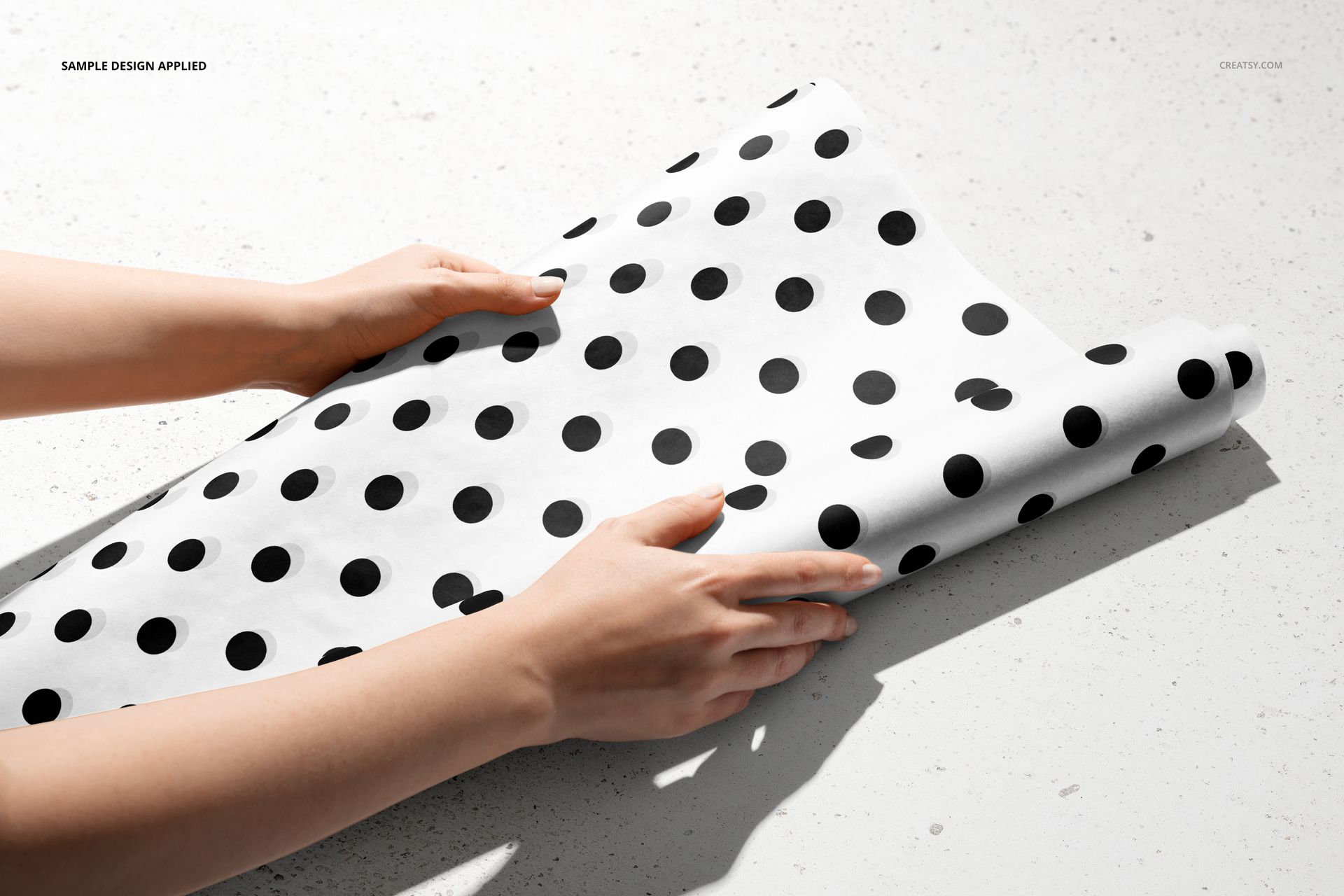 Close-up of hands arranging polka dot patterned wrapping paper, part of a packaging mockup set on a neutral background.