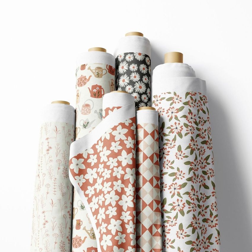 Fabric rolls mockup showing seven upright rolls with various spring-themed floral and geometric patterns on a white background.