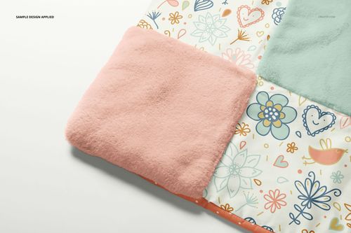 PSD mockup of a baby patchwork quilt showing pastel fleece and illustrated squares with flowers and hearts, close-up angle.