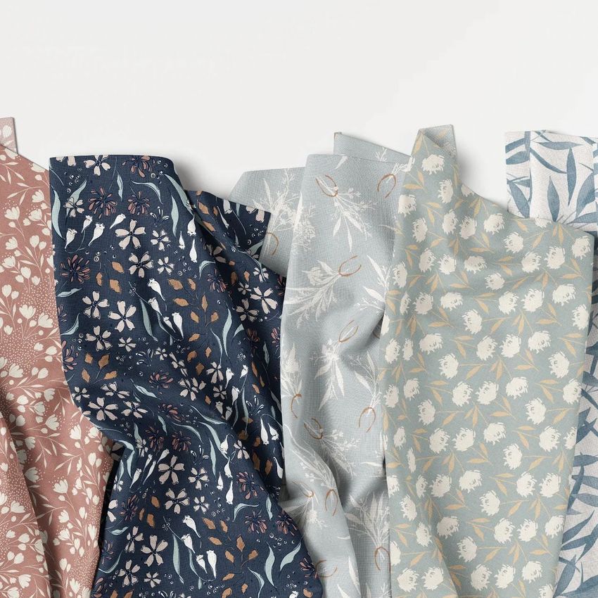 Creased fabrics mockup showing five fabric samples with floral patterns in muted shades of pink, navy, gray, and blue on a white background.