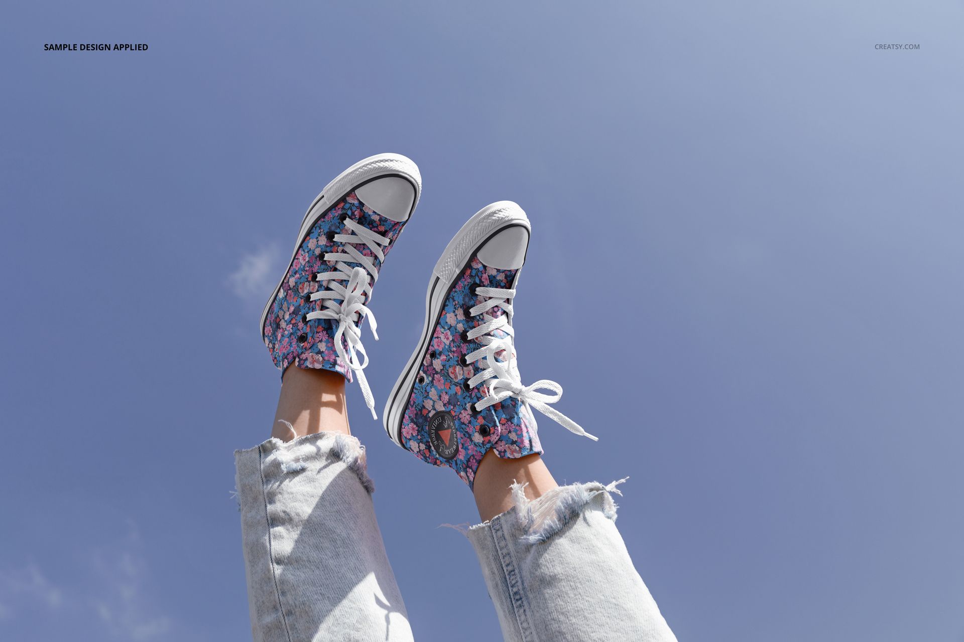 Outdoor scene showing patterned sneakers on legs in light denim jeans, with bright sky background and visible mockup details.