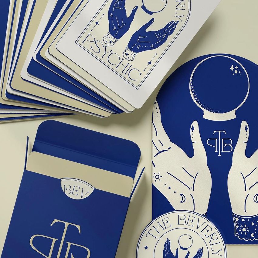 Playing cards mockup featuring blue and cream cards with mystical hand and crystal ball illustrations, arranged on a light surface.