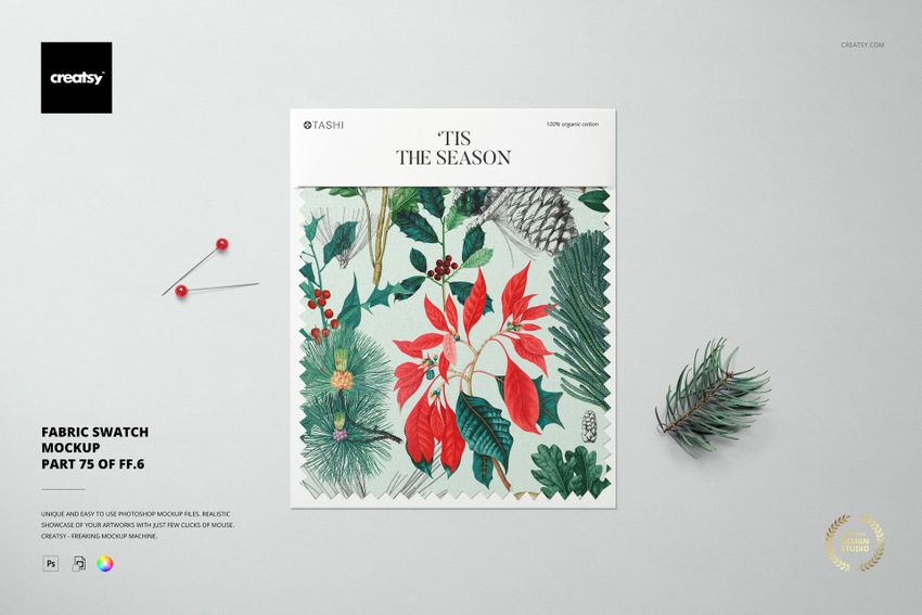 Square fabric swatch mockup with botanical holiday pattern, shown from above on a light surface with two pins and a pine twig.