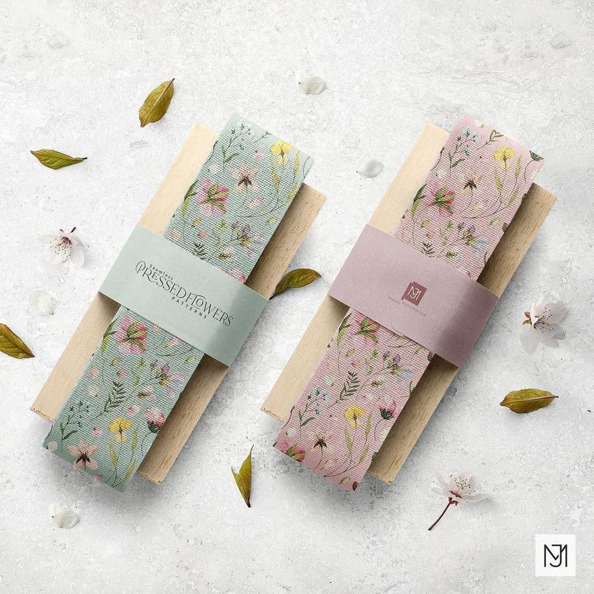 Two cotton ribbon mockups on wooden paddles, one with a blue floral pattern and one with a pink floral pattern, arranged on a light textured surface.