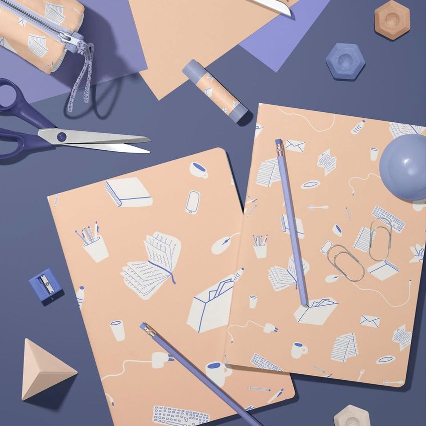 Stationery mockup featuring two classic A4 notebooks with pastel illustrated covers, surrounded by office supplies on a purple surface.