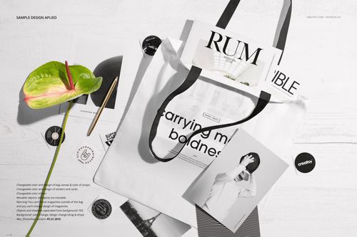 White tote bag mockup displayed on a light surface, surrounded by magazines, photographs, a pen, and a green flower.