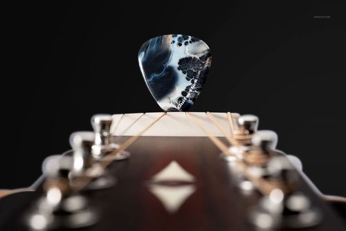 PSD mockup showing a single guitar pick with swirling colors standing between the strings on a wooden guitar headstock.