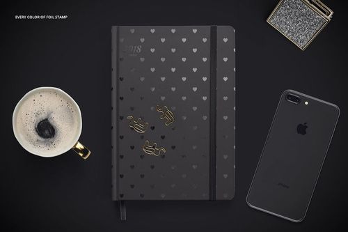 Black planner mockup with heart motifs and gold foil details, shown with coffee cup and phone on a dark background.