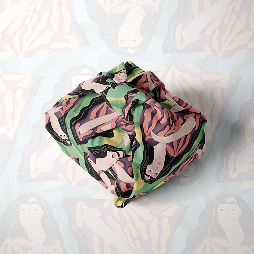 Fabric gift wrap mockup featuring a square package wrapped in cloth with an abstract illustration of a woman in earthy tones on a matching patterned background.