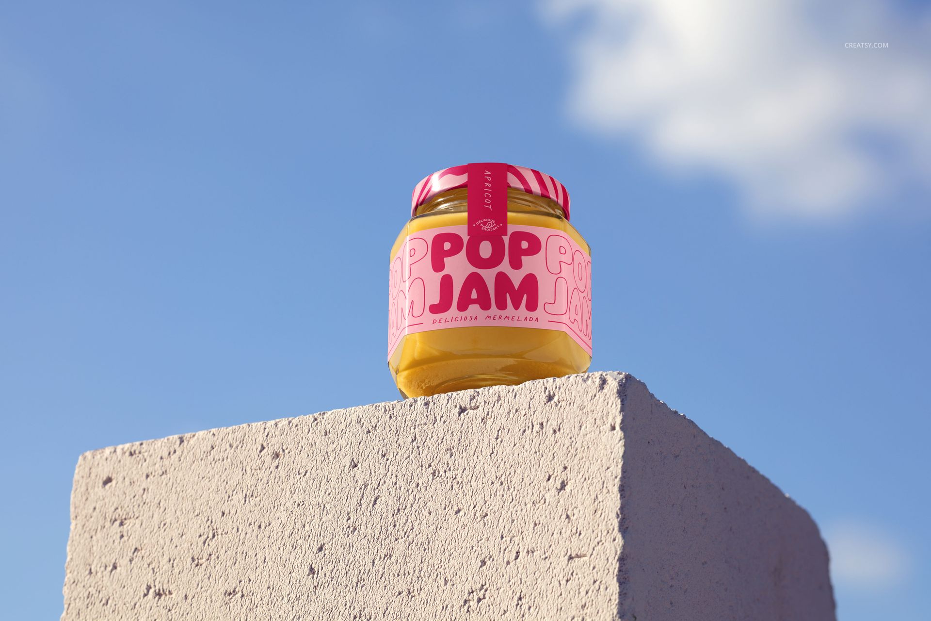PSD mockup of a jam jar with colorful packaging, displayed on a stone surface under natural daylight and open sky.