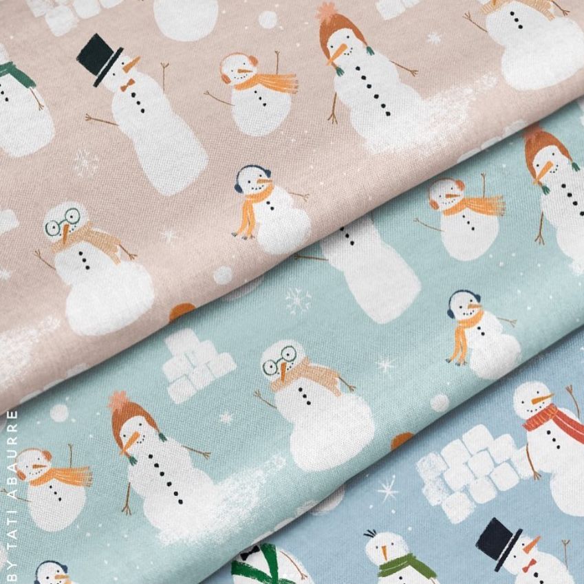 Cotton fabric mockup with three folded pieces featuring snowmen patterns in pastel pink, blue, and gray tones, seen from above.