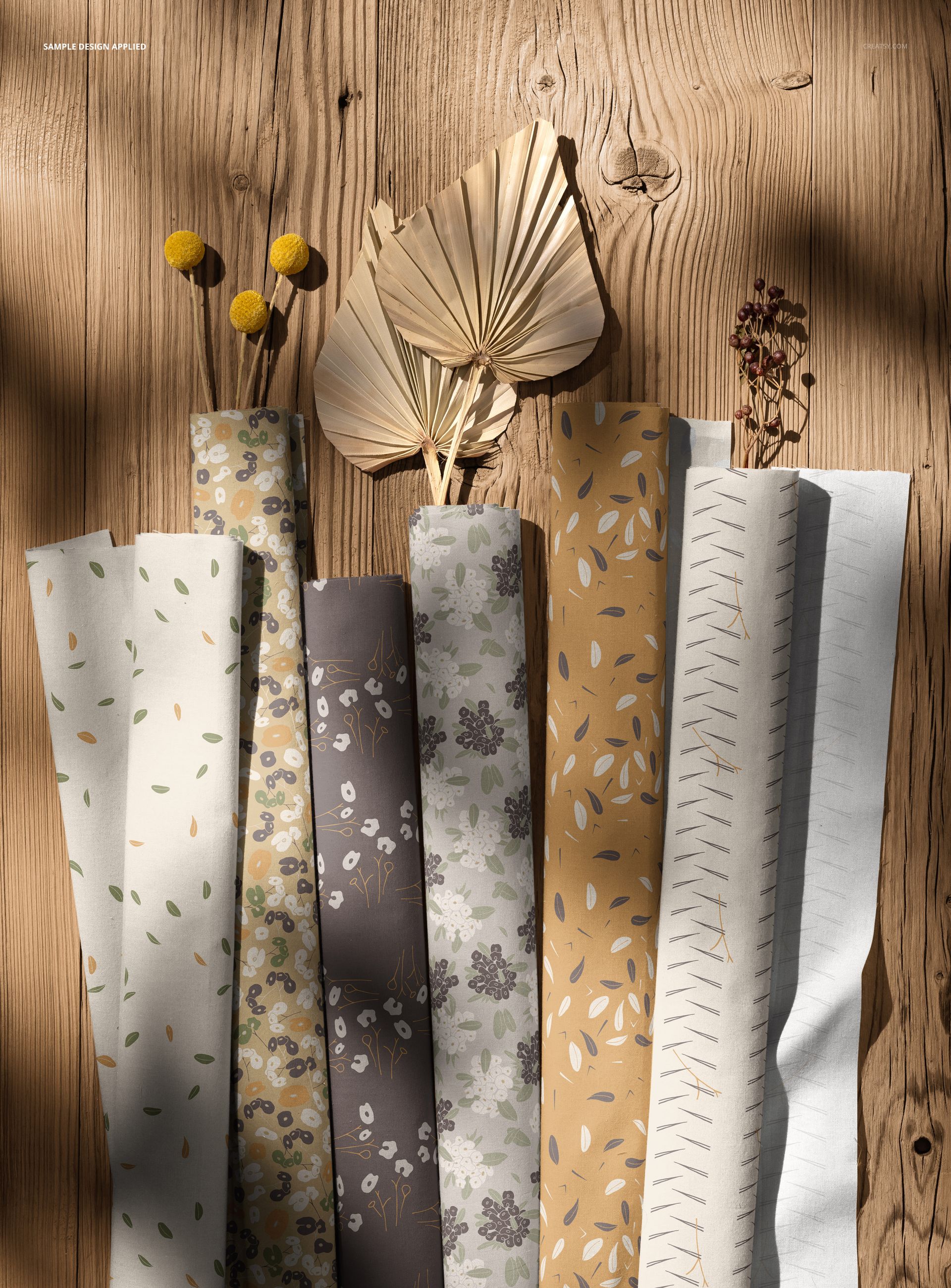 Rolled cotton fabric pieces with boho patterns in earthy tones, displayed on a wooden surface with dried flowers.