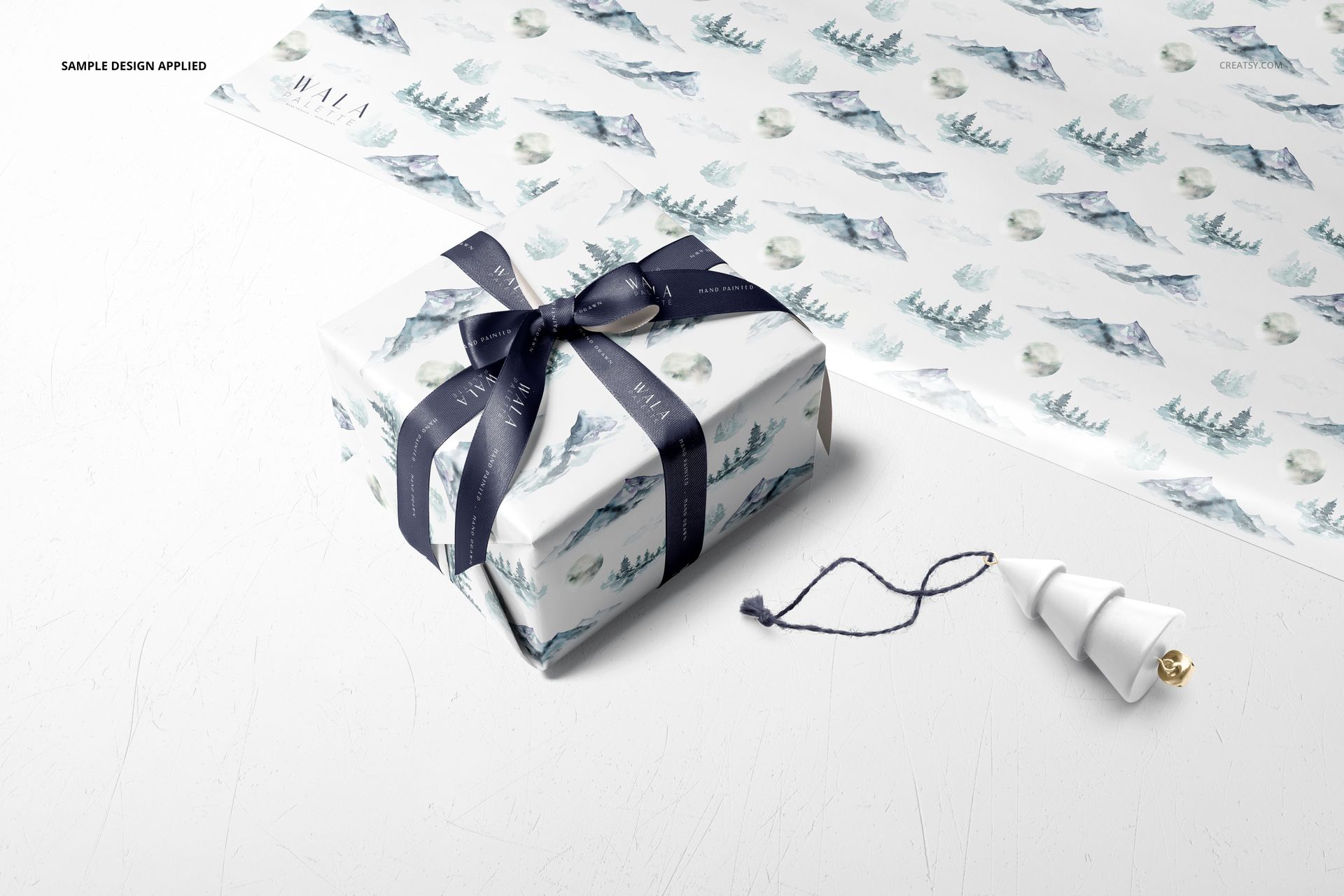 Gift wrapping paper mockup featuring a wrapped box with navy ribbon, snowy landscape pattern, and a matching sheet nearby.